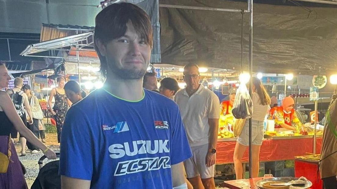 Ray Williams in a blue t-shirt, smiling in a busy street market in Thailand.