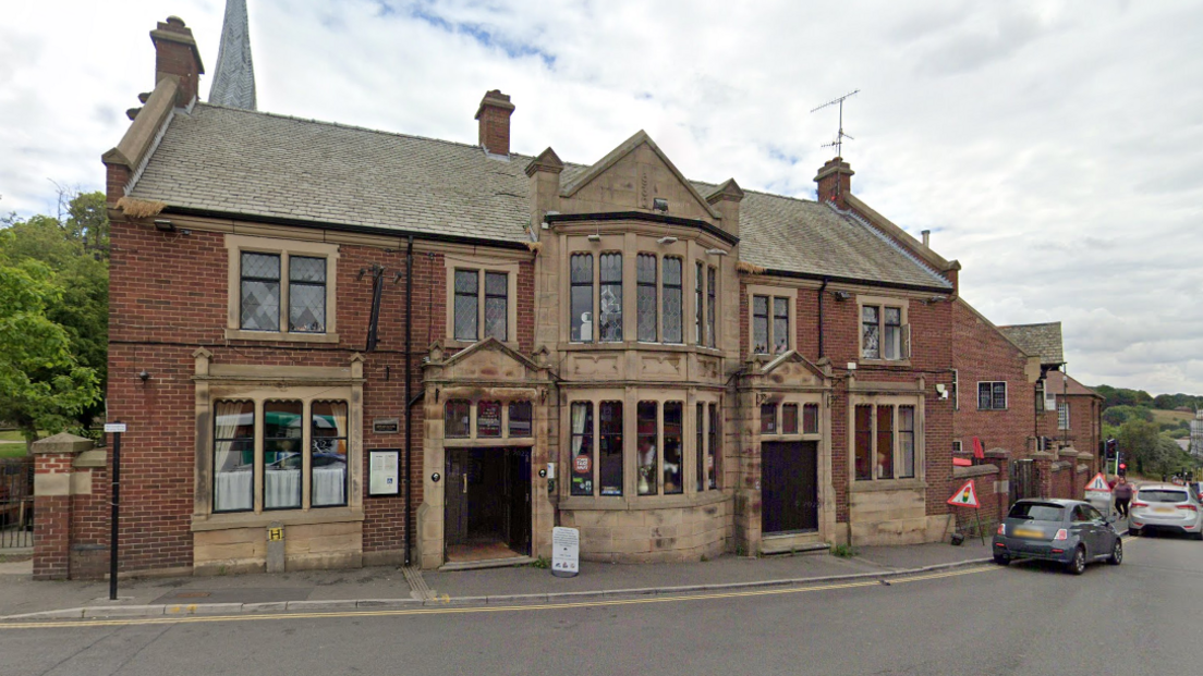 A large two-storey brick pub with Chesterfield's twisted church spire in the background