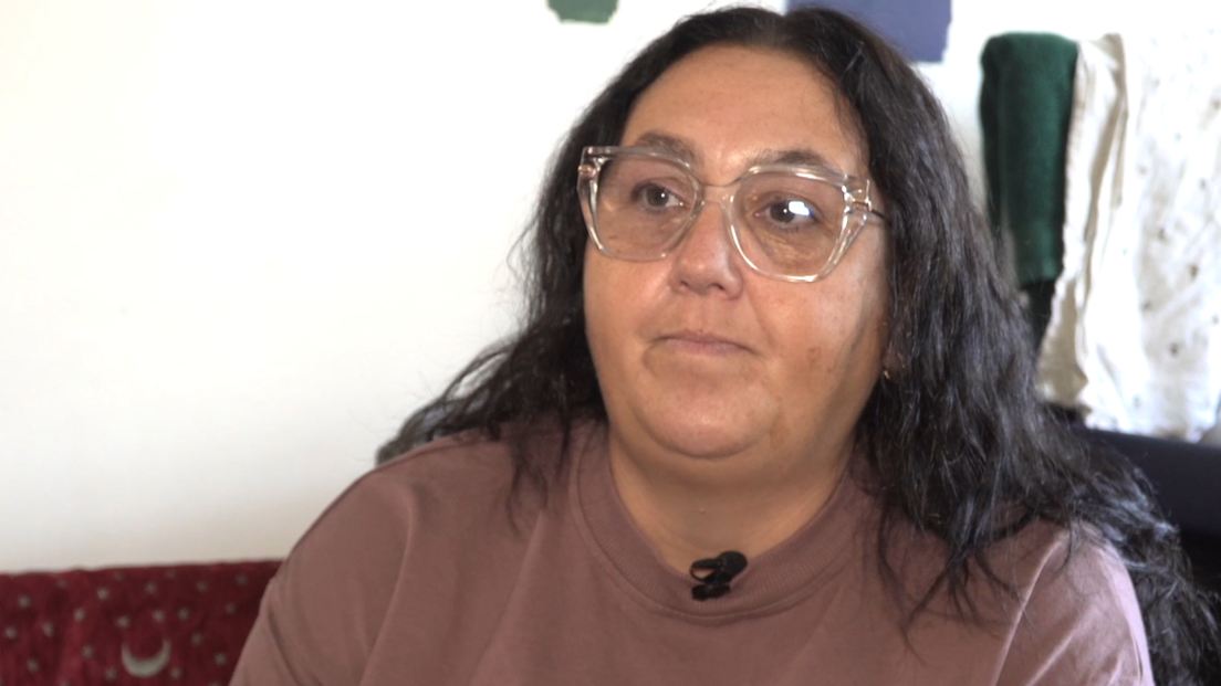 A woman with long black hair and clear glasses. She is wearing a light brown shirt and looking to the left of the screen