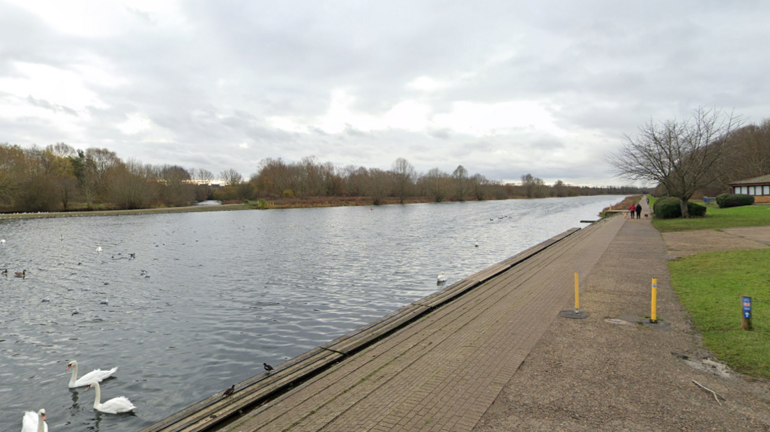 image shows a large body of water containing swans and a long parallel brick path on the right hand side 