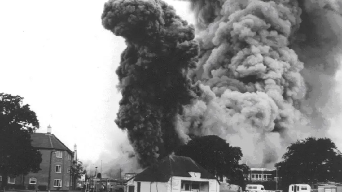 A black and white photo showing a large plume of smoke coming away from a factory.