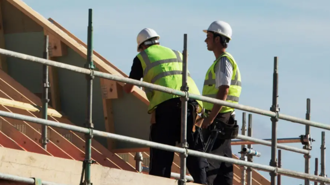 Two workmen standing on scaffolding looking at the roof of a house