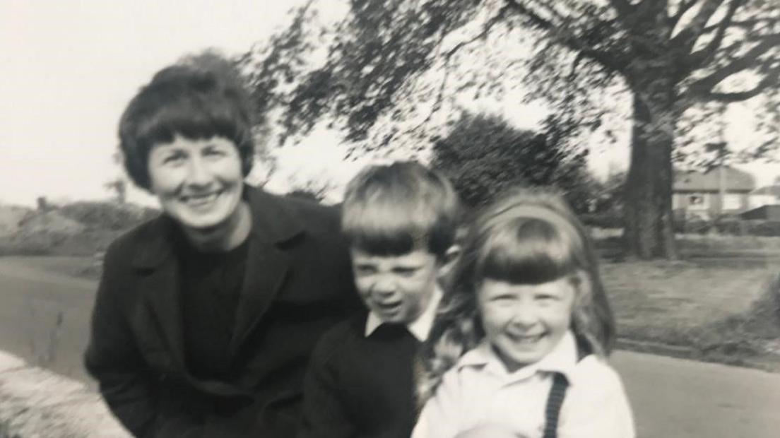 A black and white image of a smiling woman with two young children 