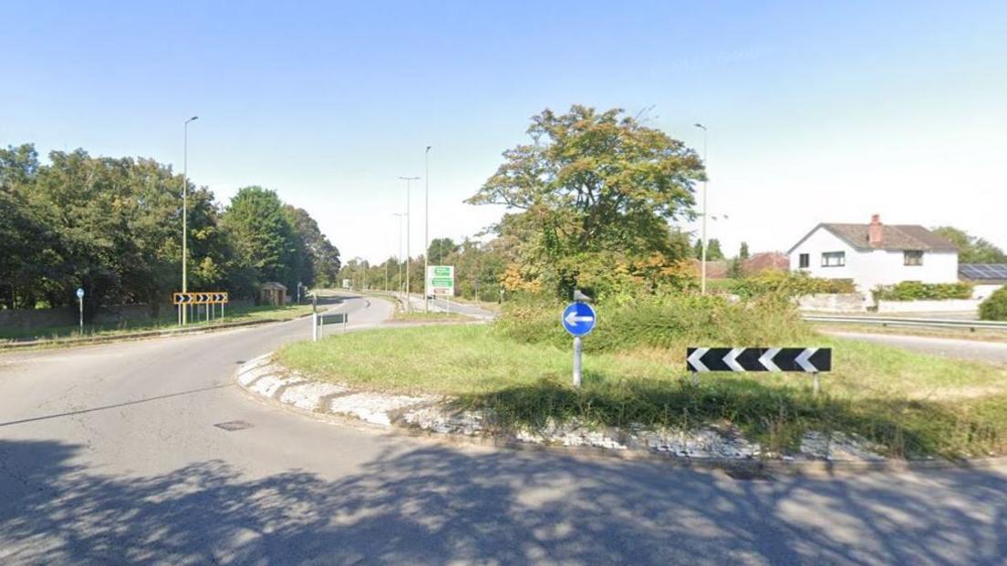 The roundabout junction on the A44 with Spring Hill Road in Begbroke. The roundabout has grass on it with a tree in the middle.