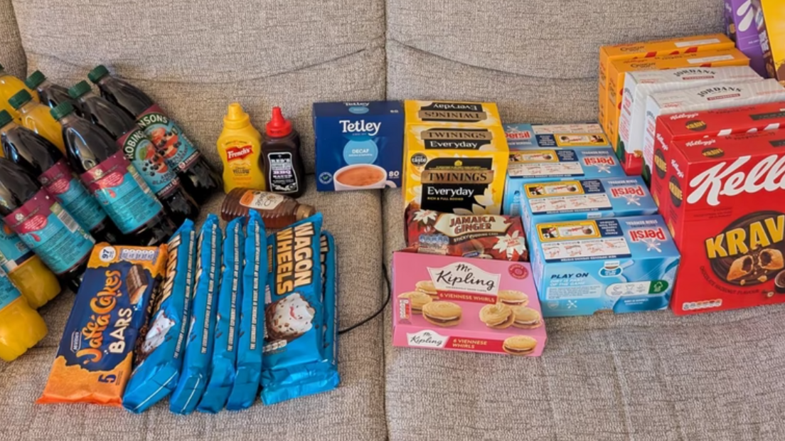 A sofa with lots of products on it, ranging from pastries and biscuits to cereal and teabags