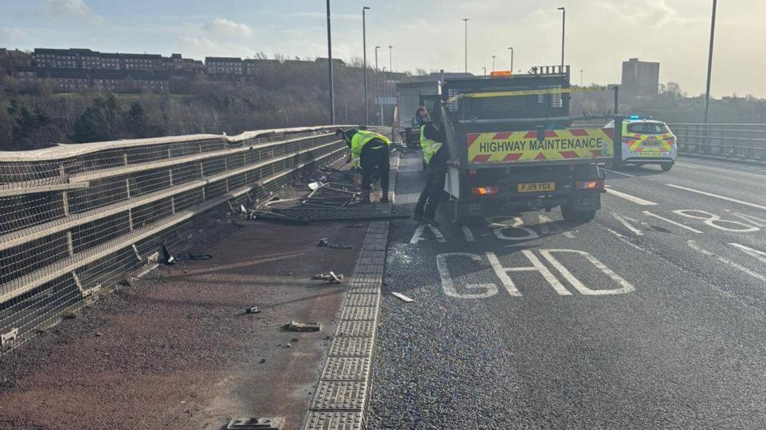 Workers in hi-vis jackets are working on the guardrail of Redheugh Bridge. Sections of the metal fencing lie on the ground.