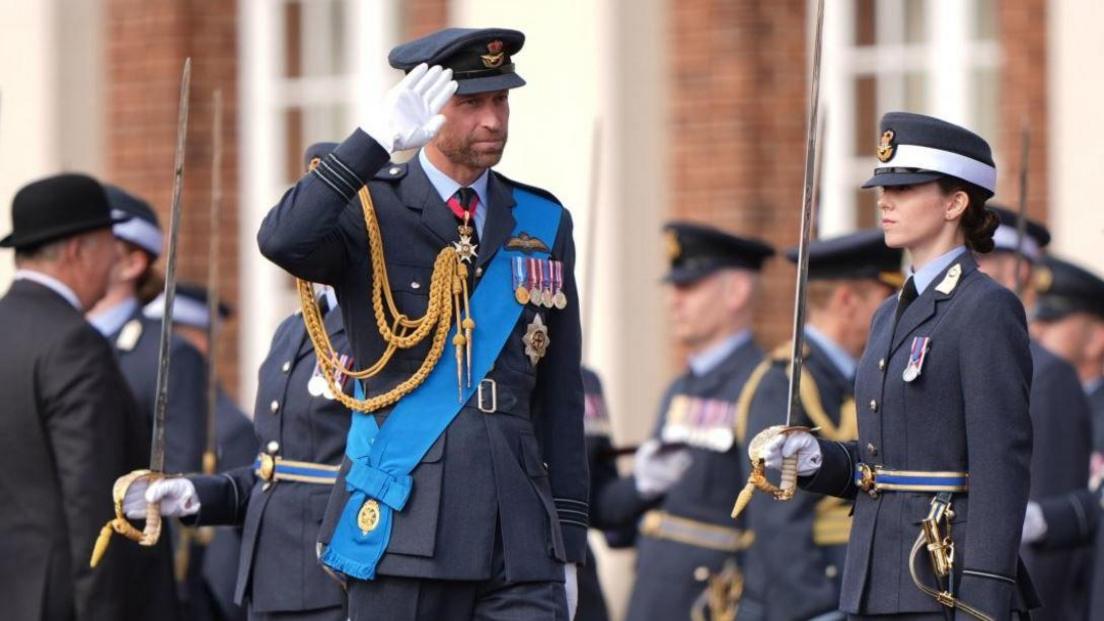 The Prince of Wales wearing an RAF uniform, walking along a line of RAF graduates and saluting