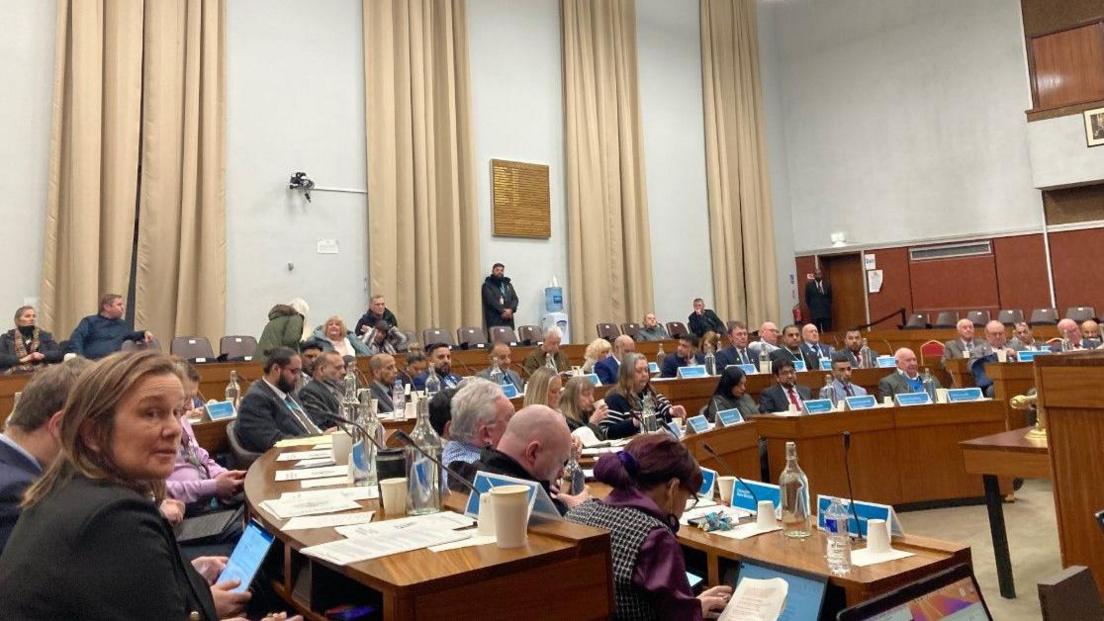 Councillors seated in the full council chamber in their circular benches