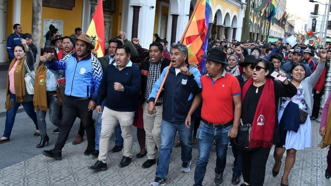 A large group of people with flags marches down a street