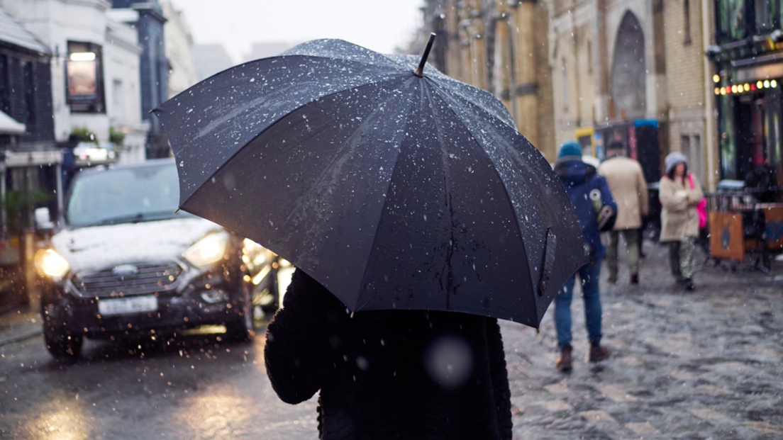 A man walks through Brighton, past the Brighton Dome, holding an umbrella in heavy rain.