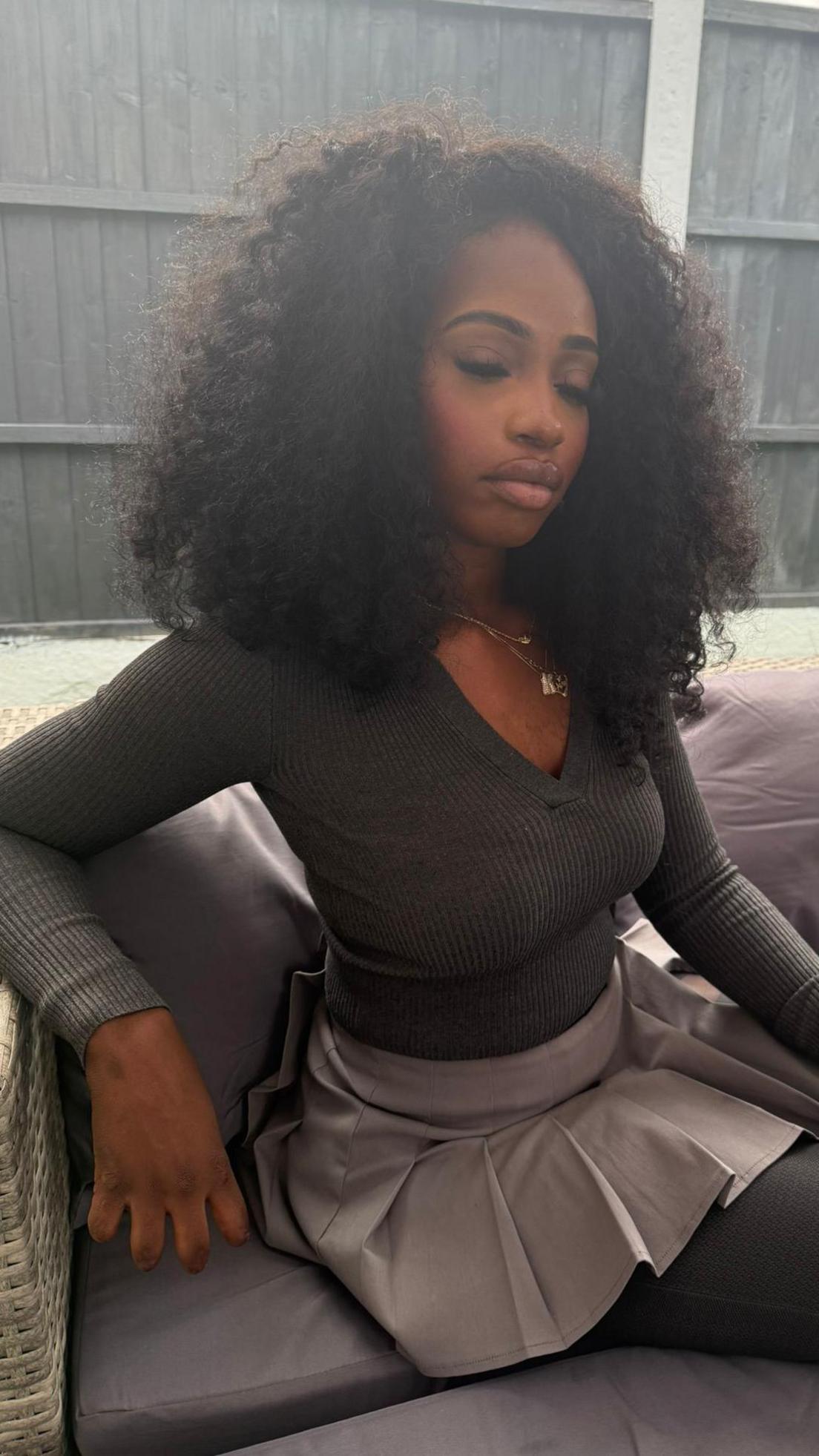 Ketia Moponda in a picture. She is wearing a grey top and a grey dress. She has dark afro-style hair. We can see she has had parts of her fingers amputated. 