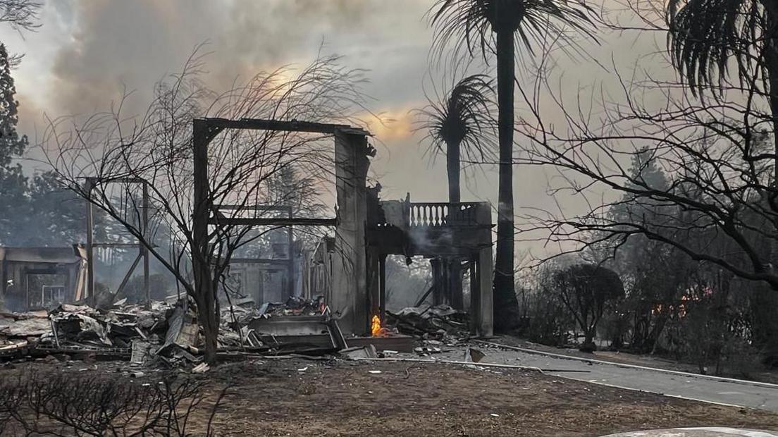 A home is pictured completely burnt following the fires. Part of the structure remains standing. Trees surrounding the home have also been burnt. Black debris can be seen around the site.