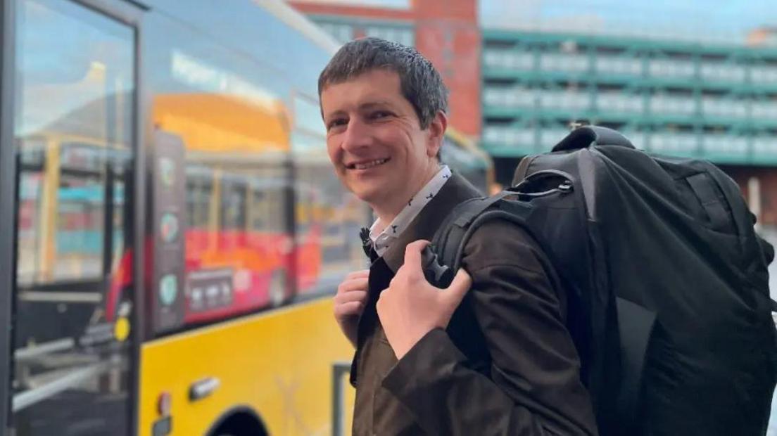 Andrew Cowell standing in front of a yellow bus in Derby bus station