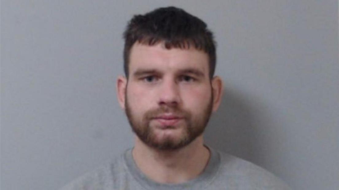 Marc Doak, pictured in custody. He has dark hair and a beard and is wearing a grey top.