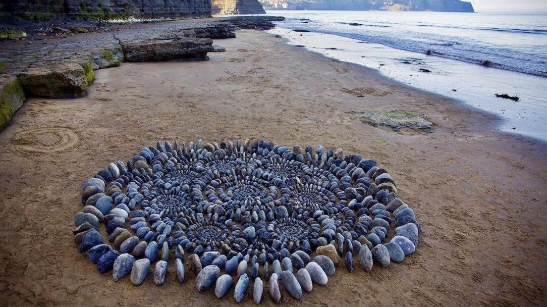 A sculpture of James Blunt's art on a beach. It is made up of grey stones and is in the shape of a flower using several hundred stones. 