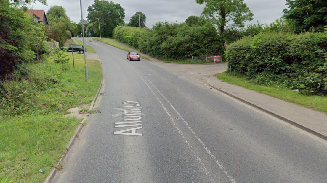 Allum Lane when it is not flooded. It shows a signpost pointing right towards the entrance of a recycling centre. A red car is driving down the hill.