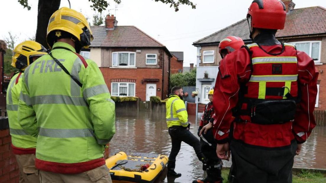 Fire crews standing in a flooded street with an empty rescue sled on the surface water