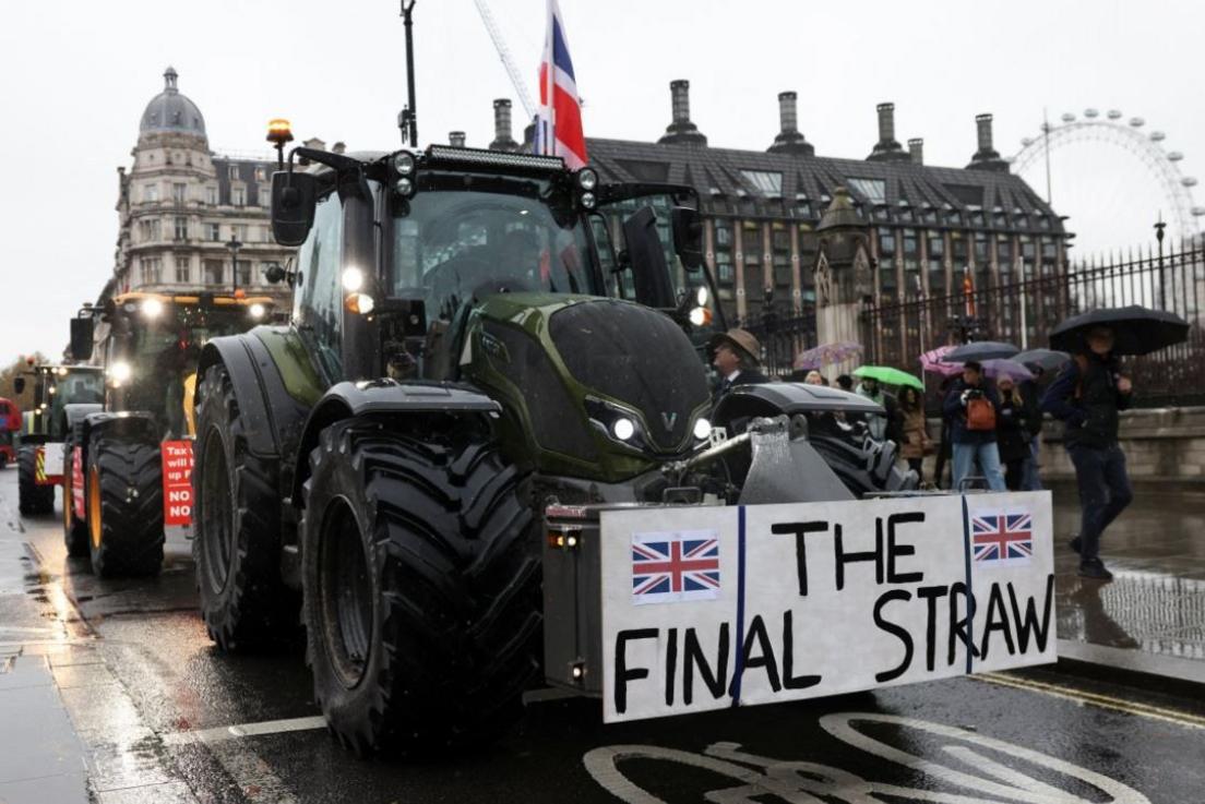 Large green tractor at the front of a number of agricultural vehicles in London. It has a placard attached to the front with the words "the final straw" written on it.