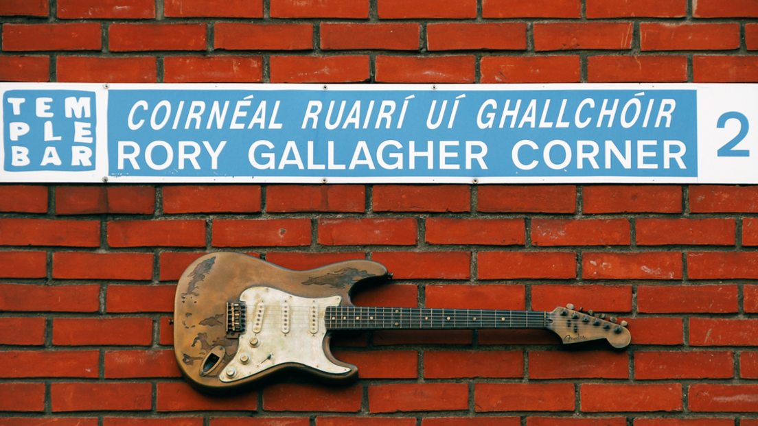 Guitar and blue and white Rory Gallagher Corner street sign on red brick wall in Dublin's Temple Bar area