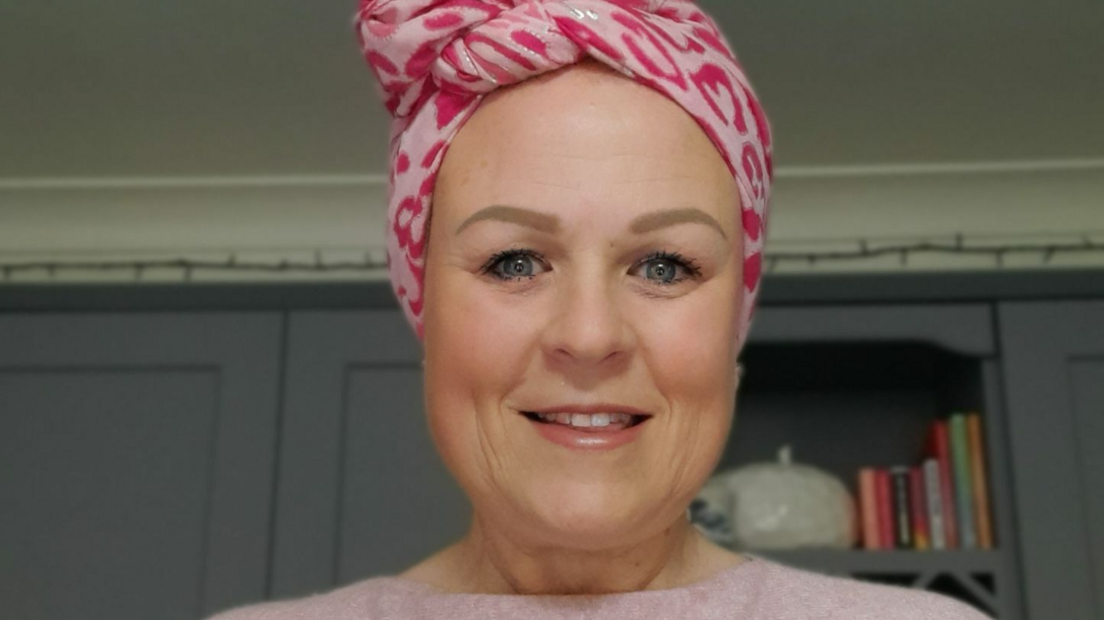 A woman with a pink headscarf and pale pink jumper smiles