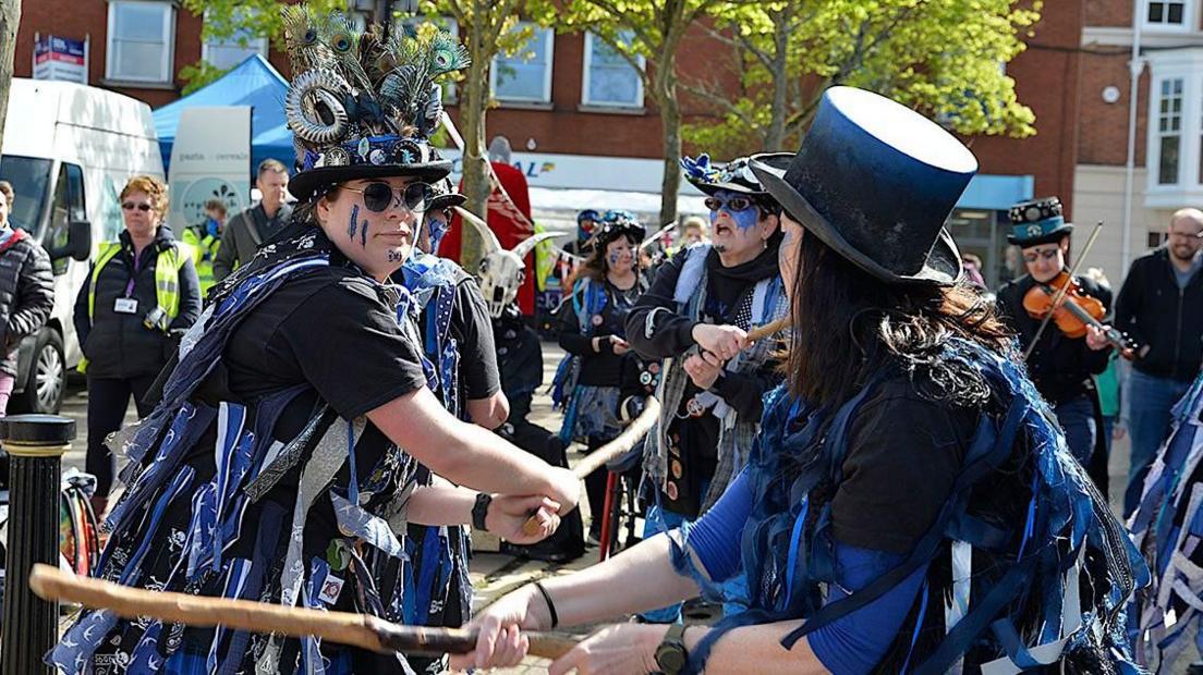 Morris dancers in blue and dark clothing with sticks