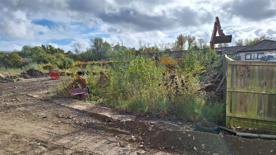 Weedy and muddy scrubland on the current site with a digger in the background