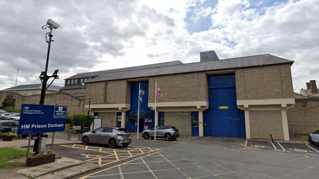 Exterior of HMP Durham. It it is a large building made of light brown bricks with two giant blue doors in the wall's surface.