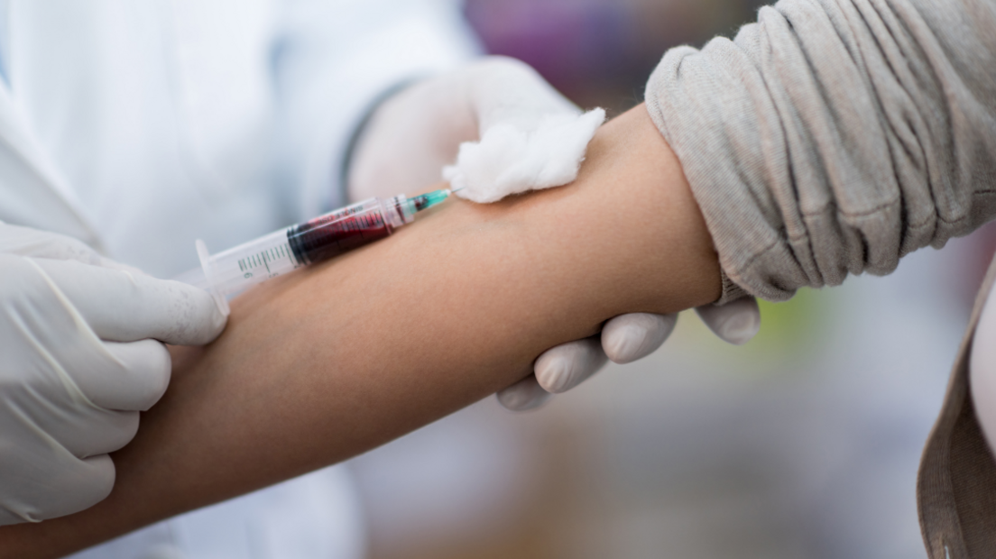 An arm presented to a nurse wearing gloves. The nurse is taking a blood sample.