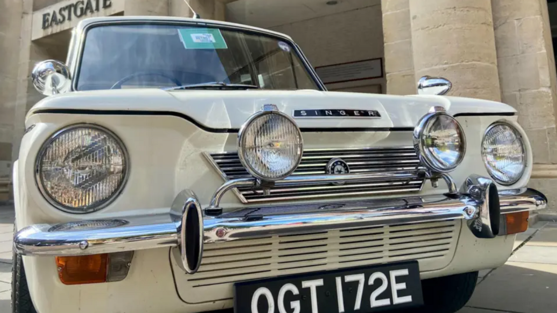 A close-up shot of a classic car, which is beige-coloured and has four large oversized headlights and a chrome bumper at the front