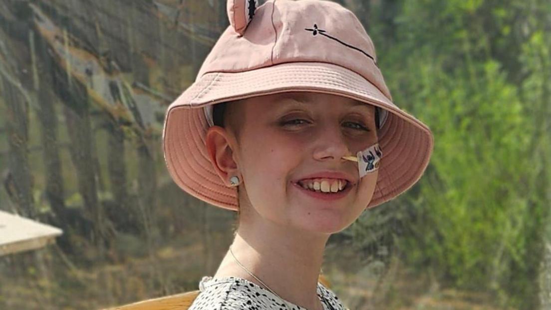 Megan. She is smiling at the camera and squinting in the sun. She is wearing a pink hat. 