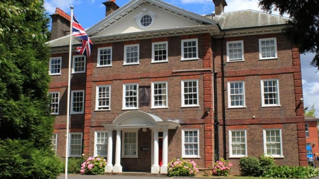 The outside of Royal Grammar School, a large red-brick building with glass-panelled sash windows. It has a Union Jack flag positioned in front of the building. 