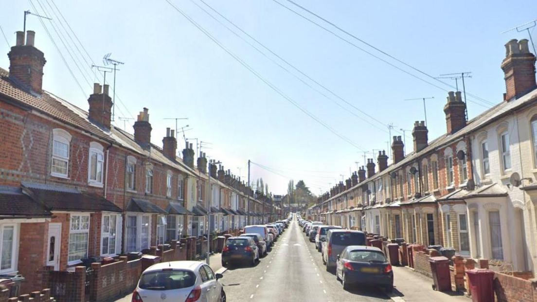 A streetview of Belmont Road. Terraced houses can be seen on both sides of the road with cars parked all down the road. The houses are a mixture of red brick and cream painted houses.