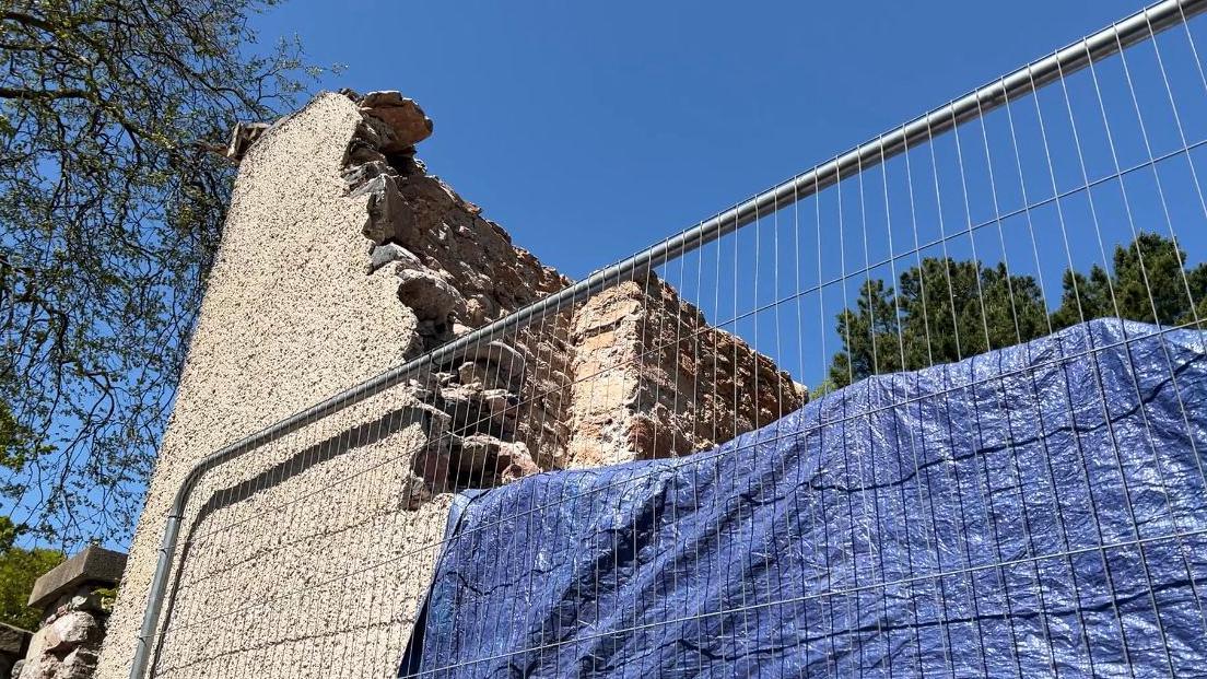 Part of the wall of Singleton Gardens has been demolished with tarpaulin over part of the wall and fencing in front of it