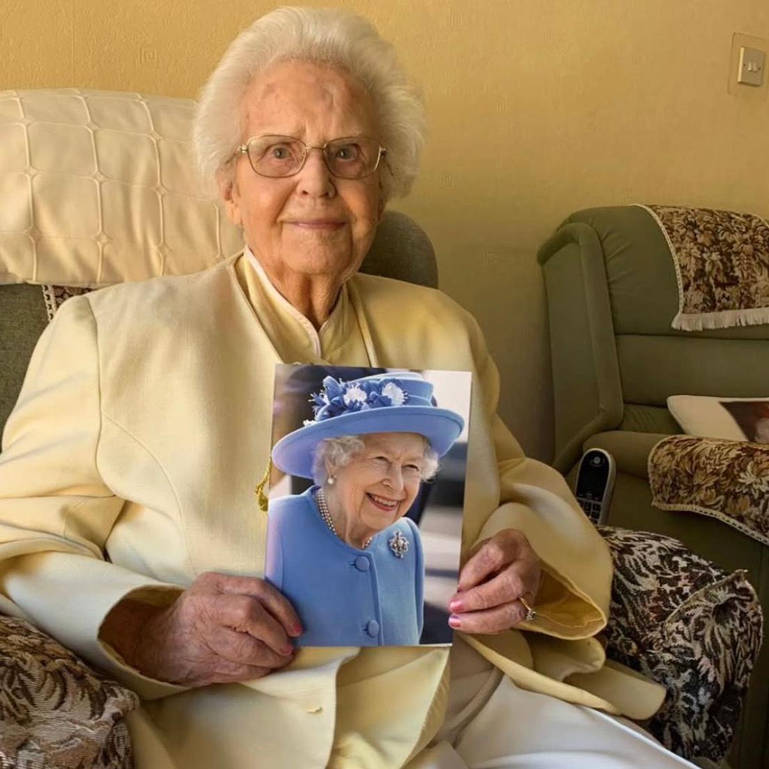 An older woman dressed smartly and holding a photo of the queen