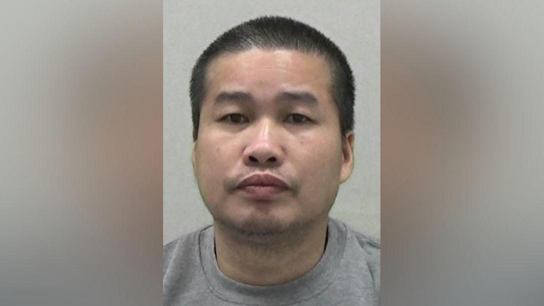 Mugshot of Le. He has short spiky shaved black hair and a very faint stubbly beard.