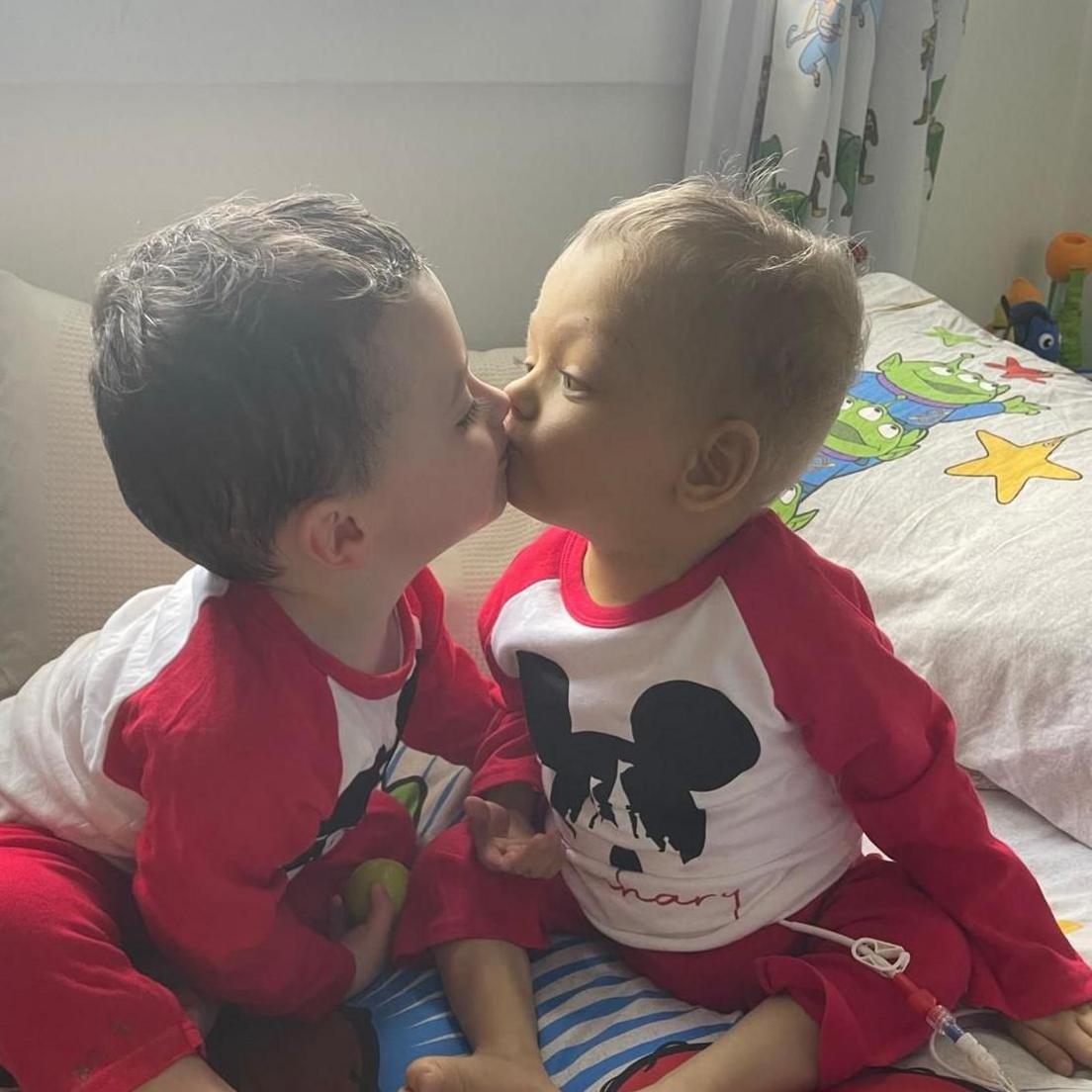 Reuben and Zachary give each other a kiss - they are both wearing red Mickey Mouse pyjamas