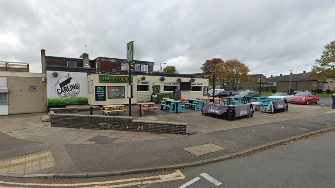 A cladded building with a sign reading "The Phoenix" and multi-coloured picnic tables outside