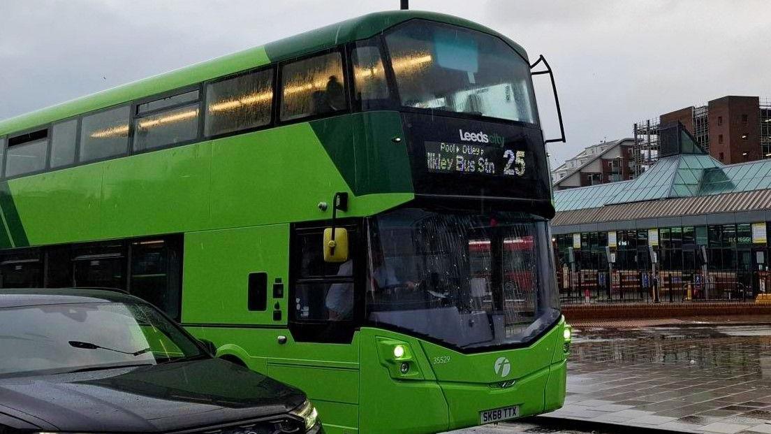 A green Leeds City bus, number 25, with part of a black car in the foreground. Leeds City Bus Station can be seen in the background.