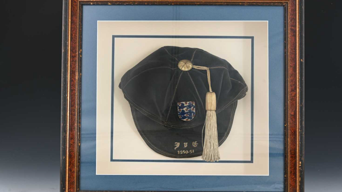 A blue velvet cap with a pale tassel, framed in a wooden picture frame.