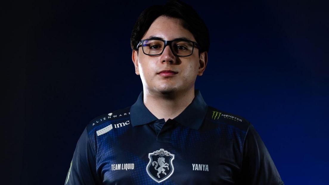 A man with black glasses has a serious expression as he looks at the camera. He's wearing a blue team polo shirt with a logo on it that has a white horse in the middle.