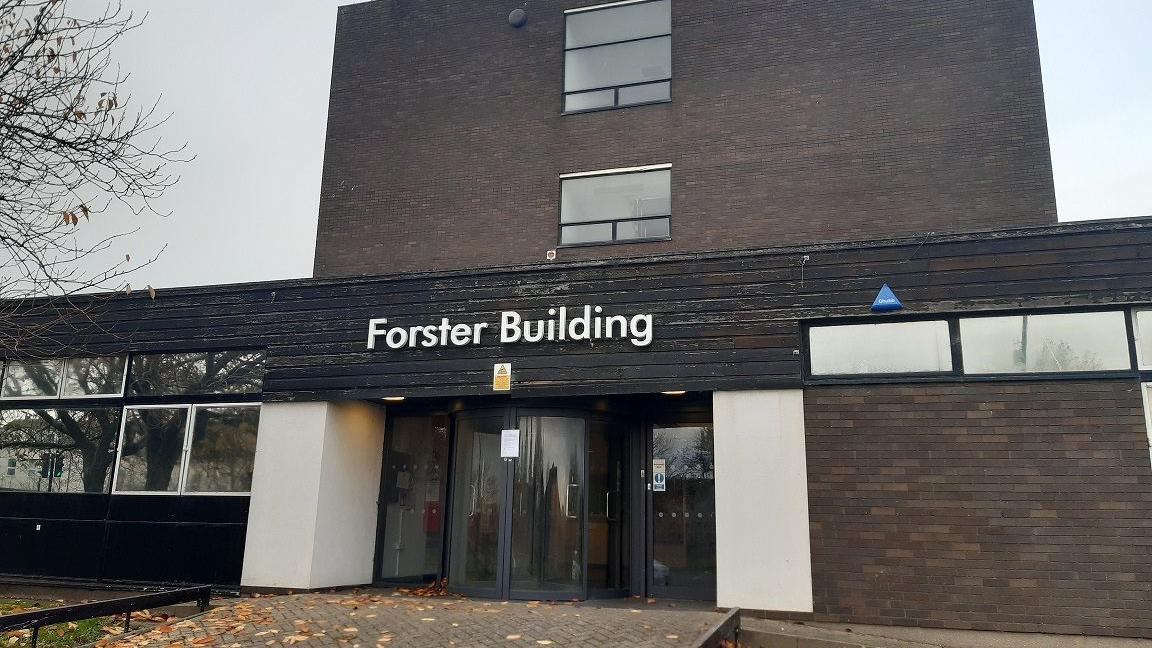 A dark brick building with glass entrance doors. The name "Forster Building" is written above the entrance in white lettering. 