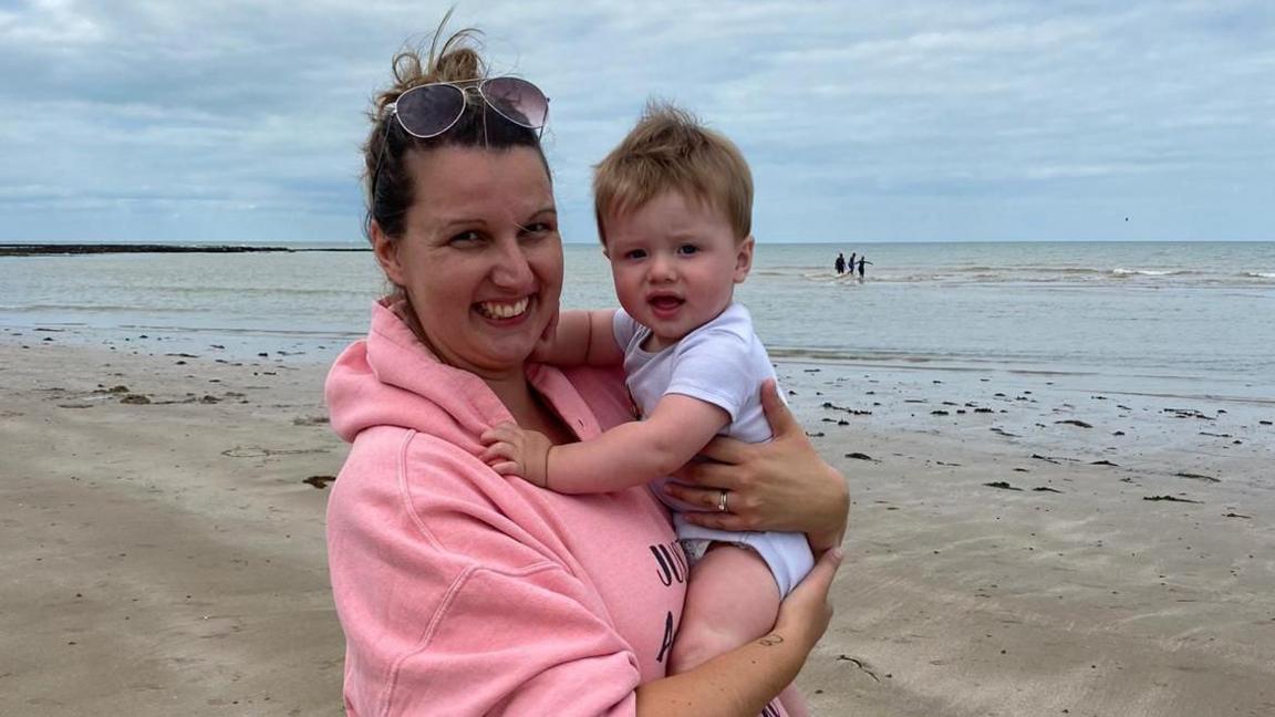 Zoe Steeper holding her son Oliver on the beach both smiling