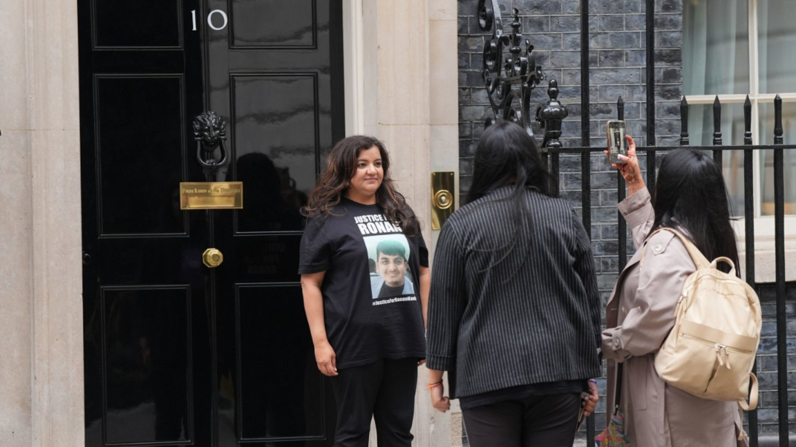 Ms Kanda is stood outside Downing Street having her photo taken by two women. She is wearing black T-shirt with her son's face on the front.