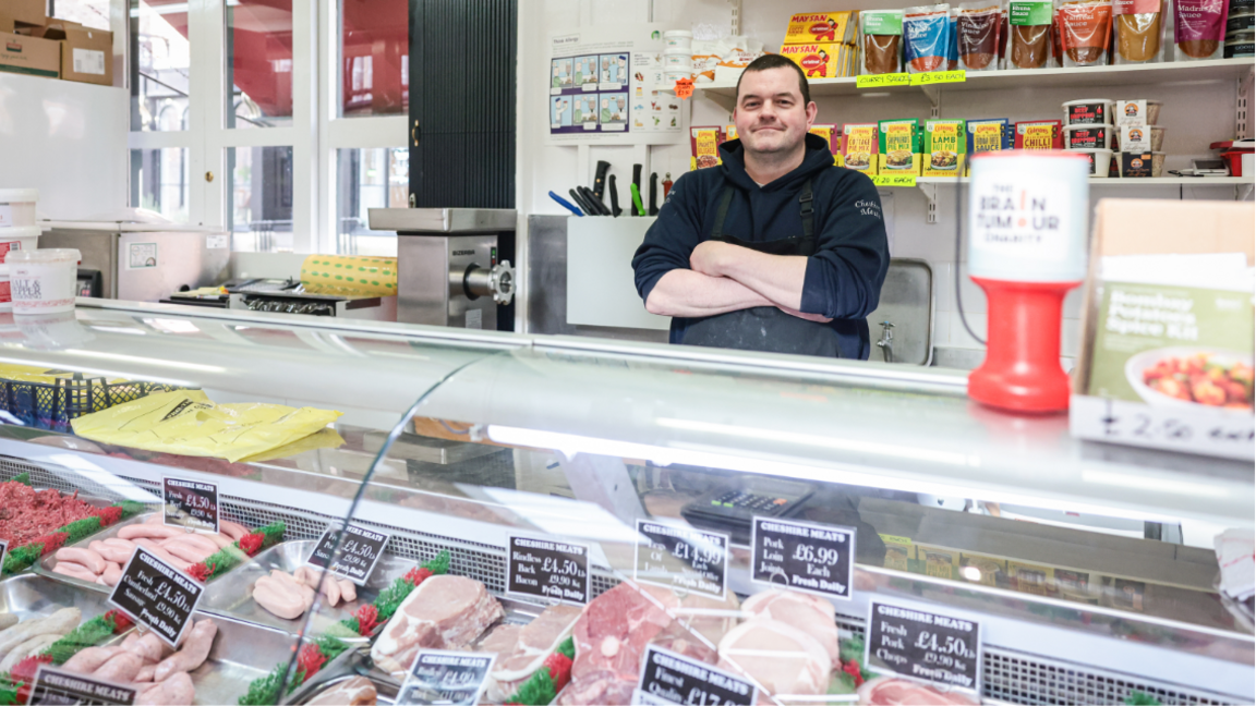 Butcher Scott Donnelley with his arms folded, smiles behind his meat counter in front of mince, sausages and bacon 