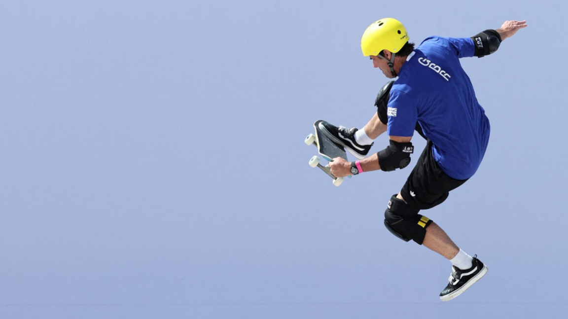 The picture shows a person skateboarding. They're equipped with full protective gear—helmet, knee pads, elbow pads, and wrist guards. 