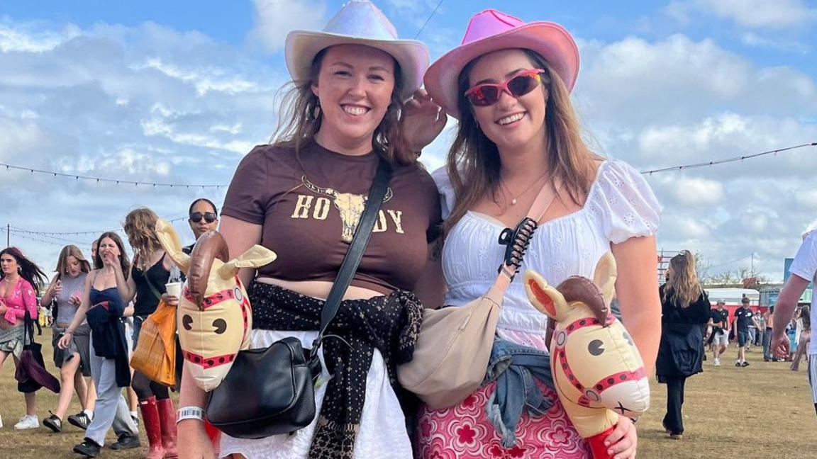 Two young women dressed in cowboy hats and each holding an inflatable hobby horse