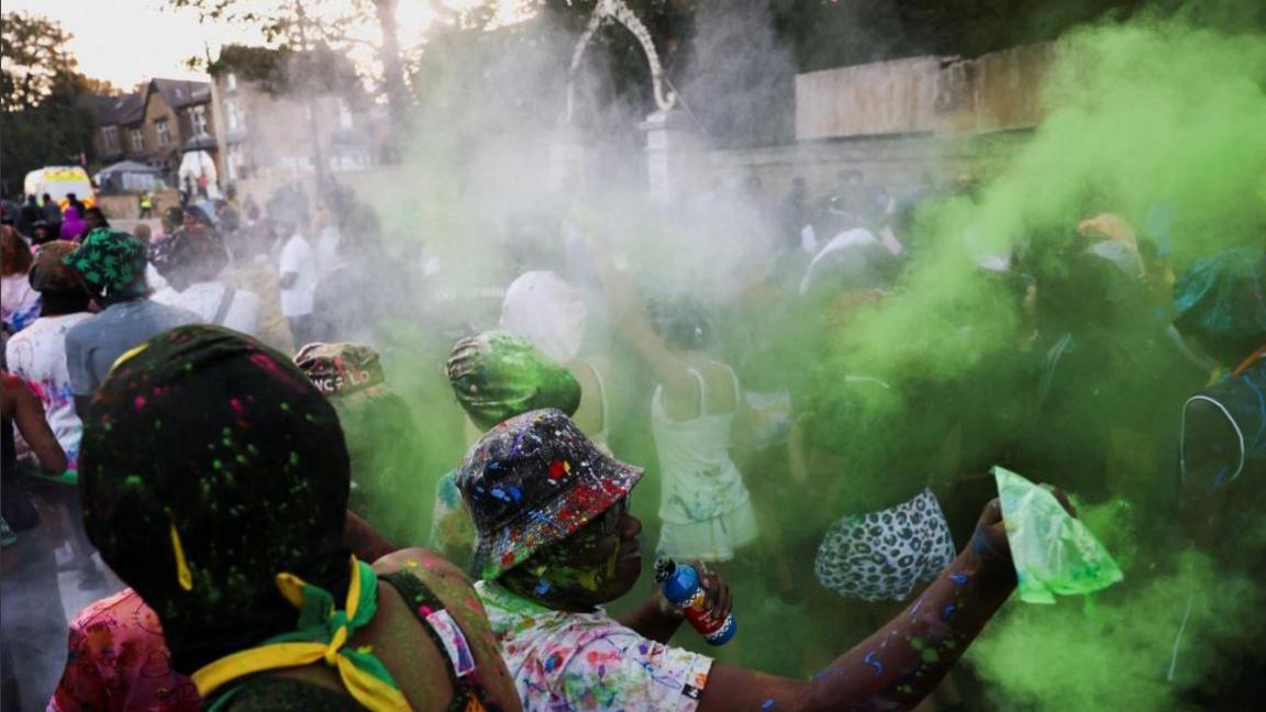 People taking part in J'Ouvert celebrations before Leeds West Indian Carnival 2025, with smoke, coloured powder and costumes