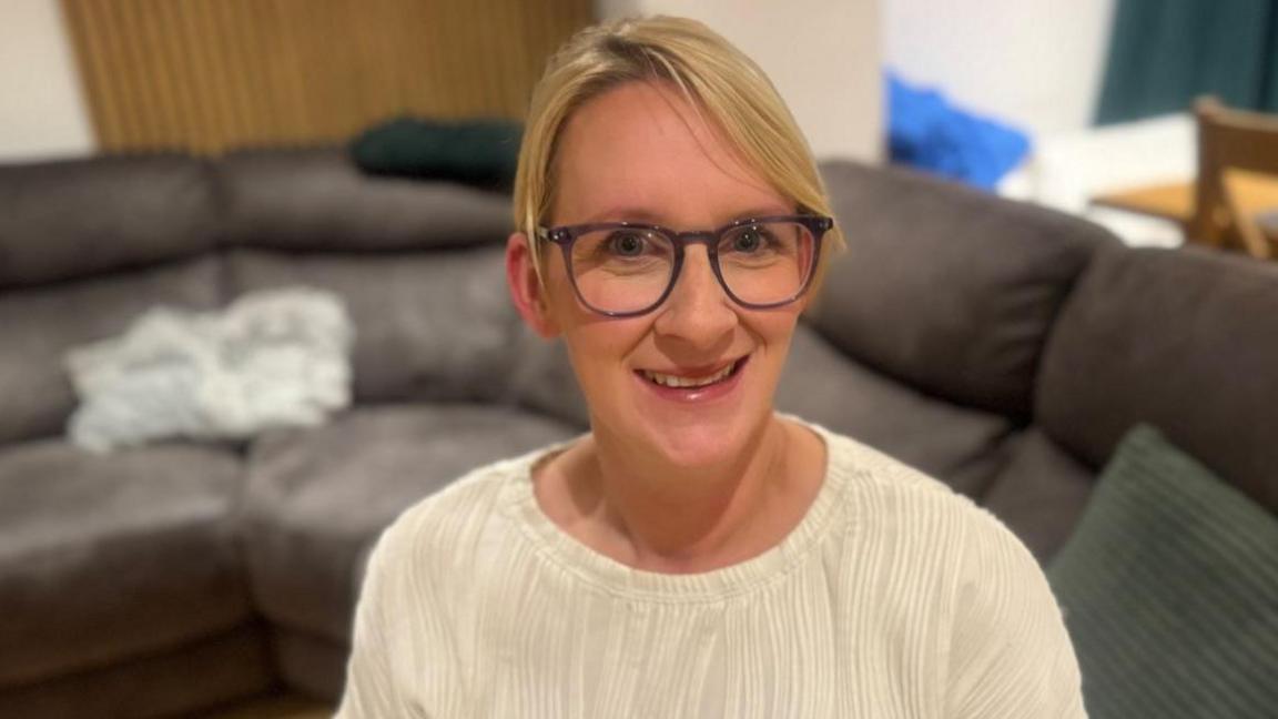 Mared Jones in a white top and glasses smiles at the camera. It is a head and shoulders shot.
