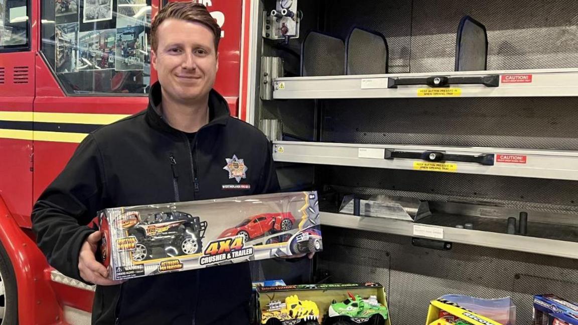 A firefighter holding a toys in front of a fire engine