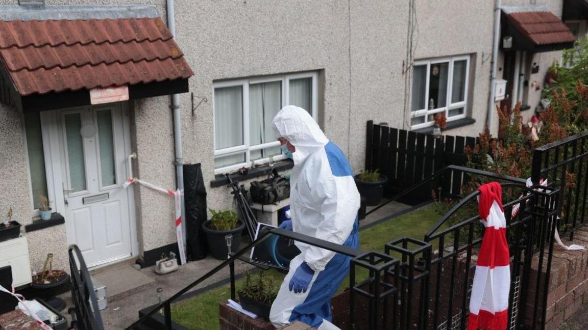 An individual in a forensic protective suit is walking into a property